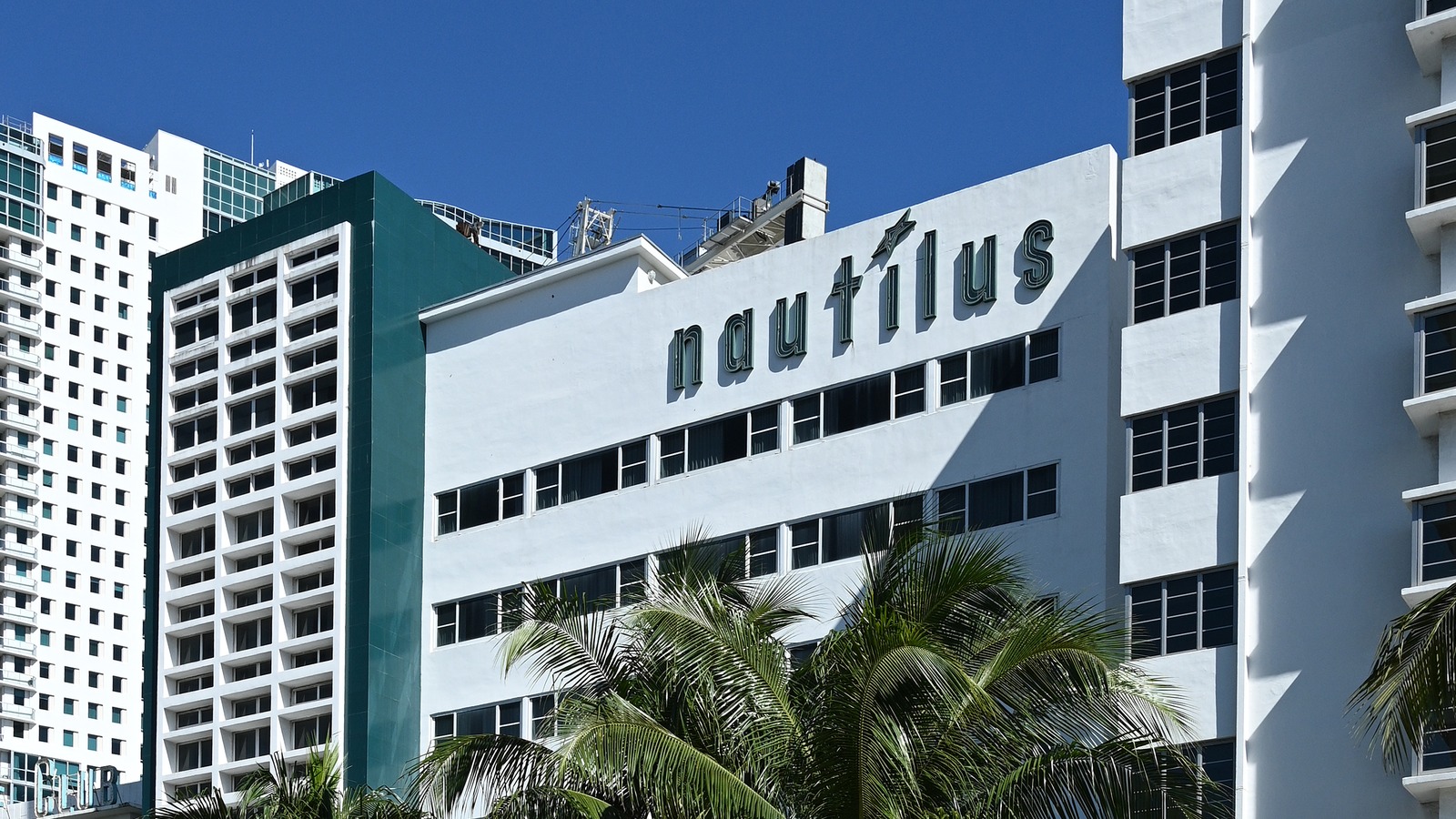 The white Nautilus hotel building with rooftop signage on Collins Avenue in Miami Beach, framed by palm trees on a clear day