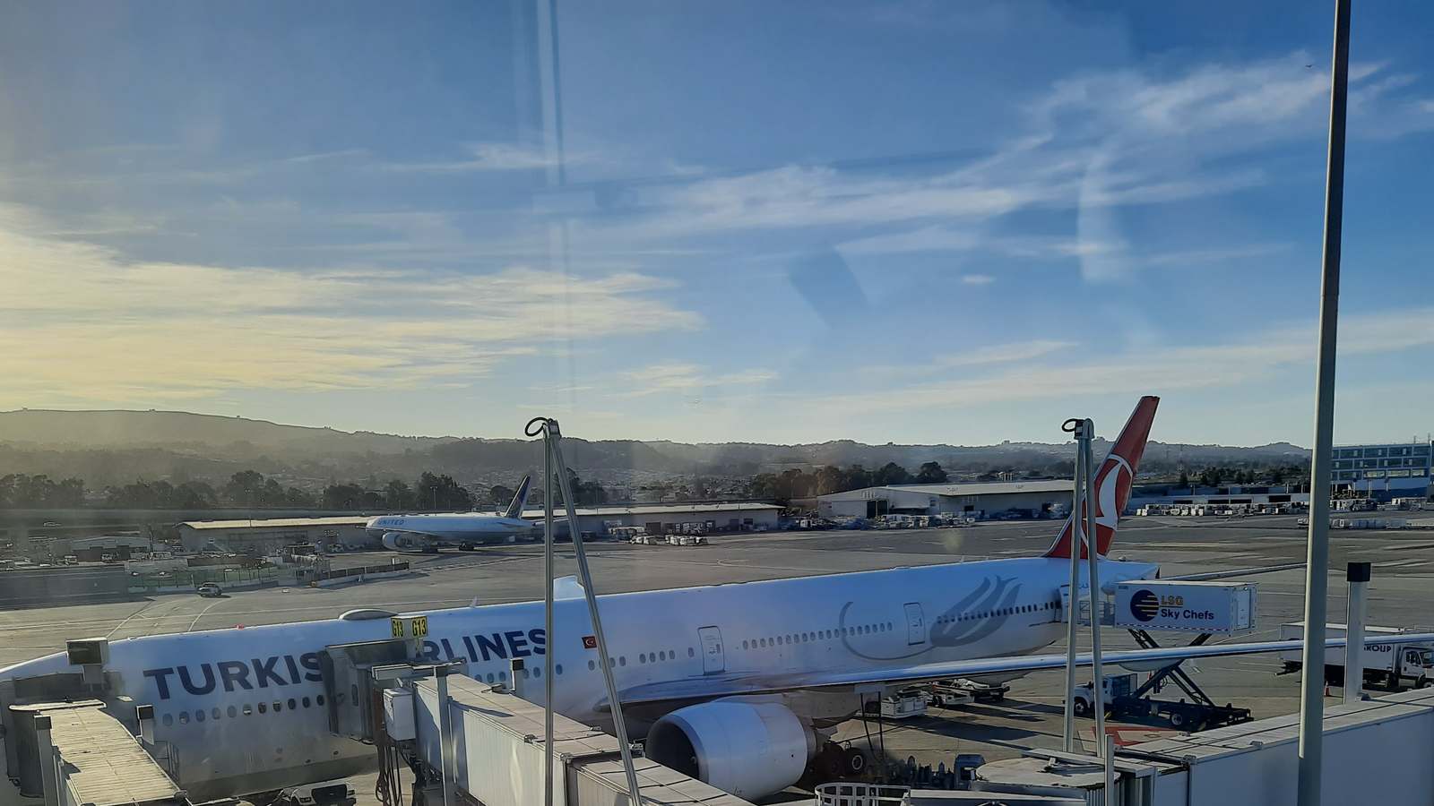 A Turkish Airlines widebody jet parked at a gate at San Francisco International Airport, seen through a terminal window.