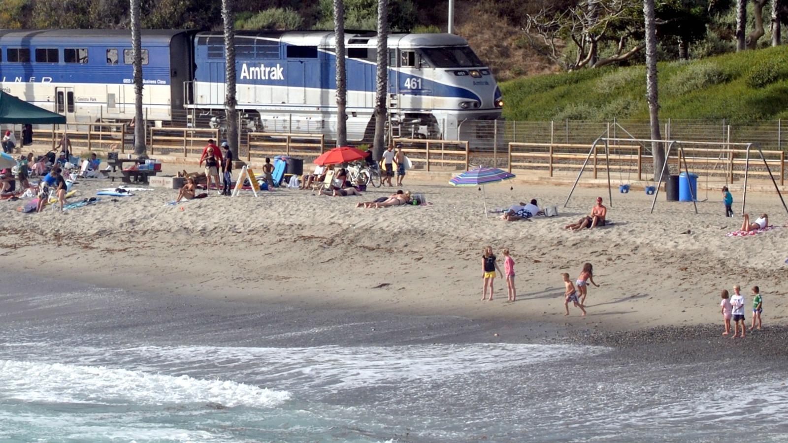 Pacific Surfliner train passing San Clemente Beach as people sit on the sand beside the ocean