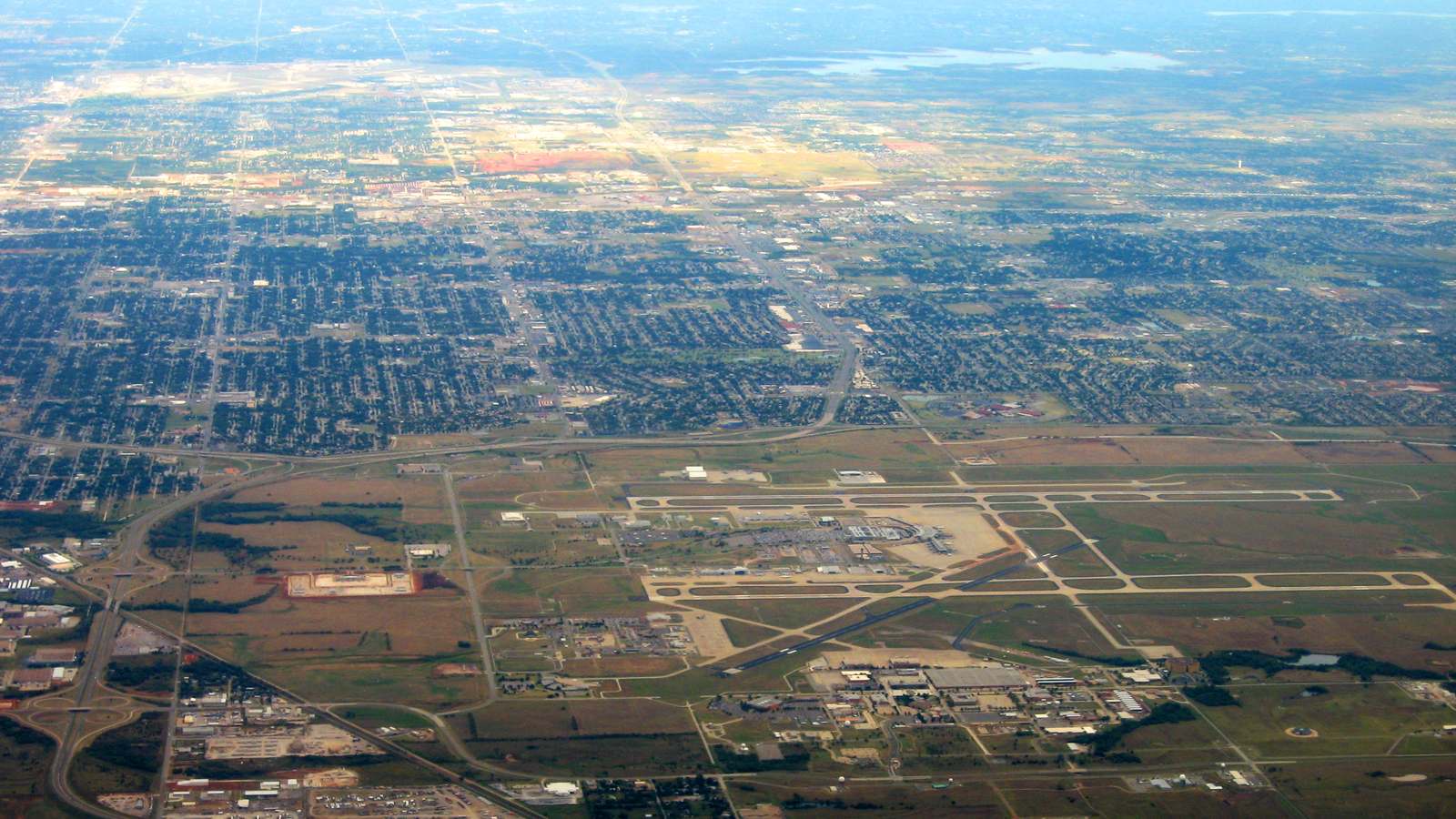 An aerial view of Will Rogers airport in Oklahoma City, with runways, terminal and surrounding neighborhoods stretching to the horizon.