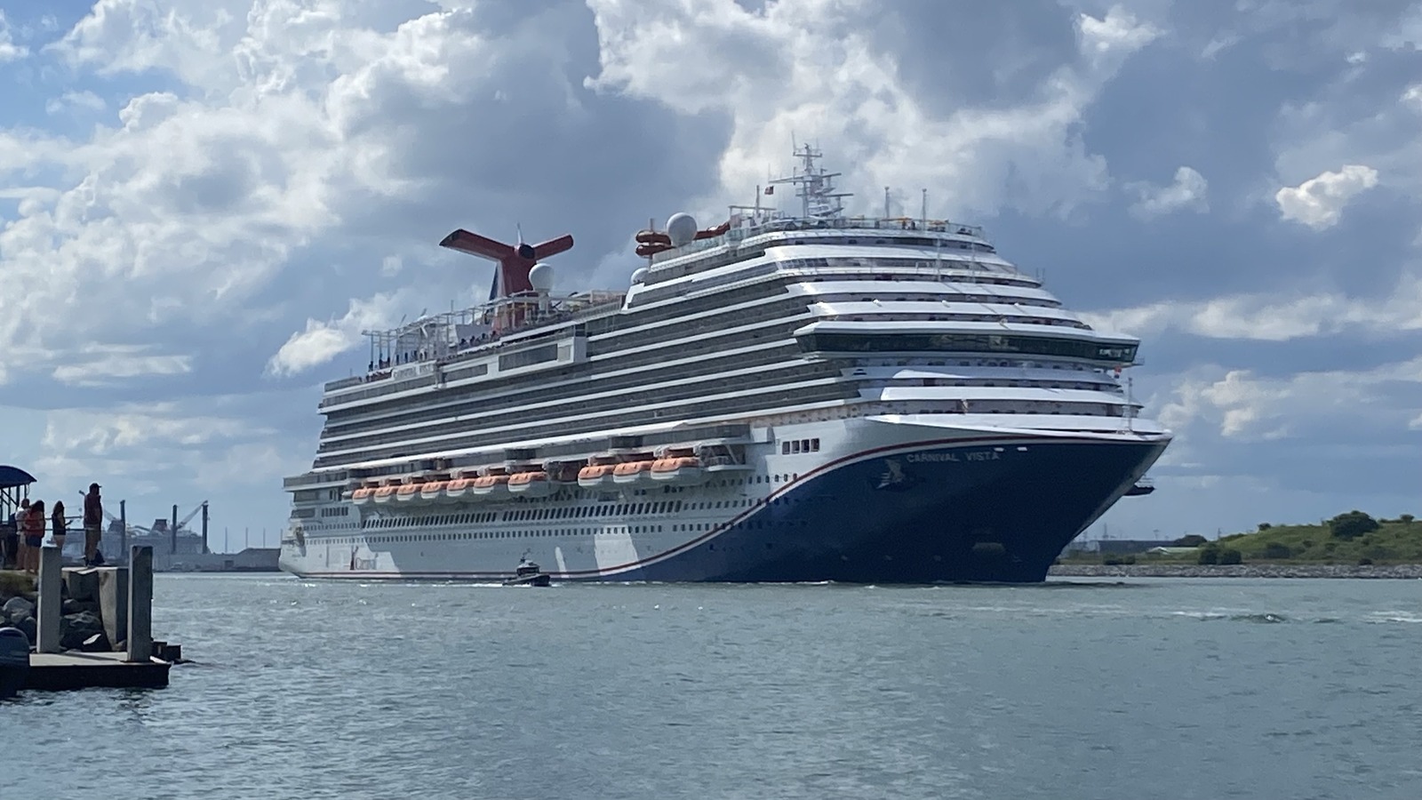 Carnival Vista departing Port Canaveral under a partly cloudy sky, with the ship's name visible on the bow