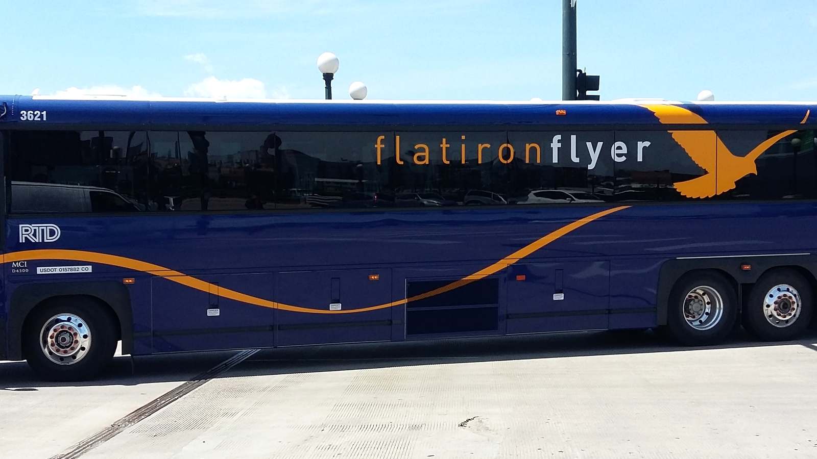 An RTD Flatiron Flyer coach bus in blue and orange livery parked at a Denver stop under a clear sky.