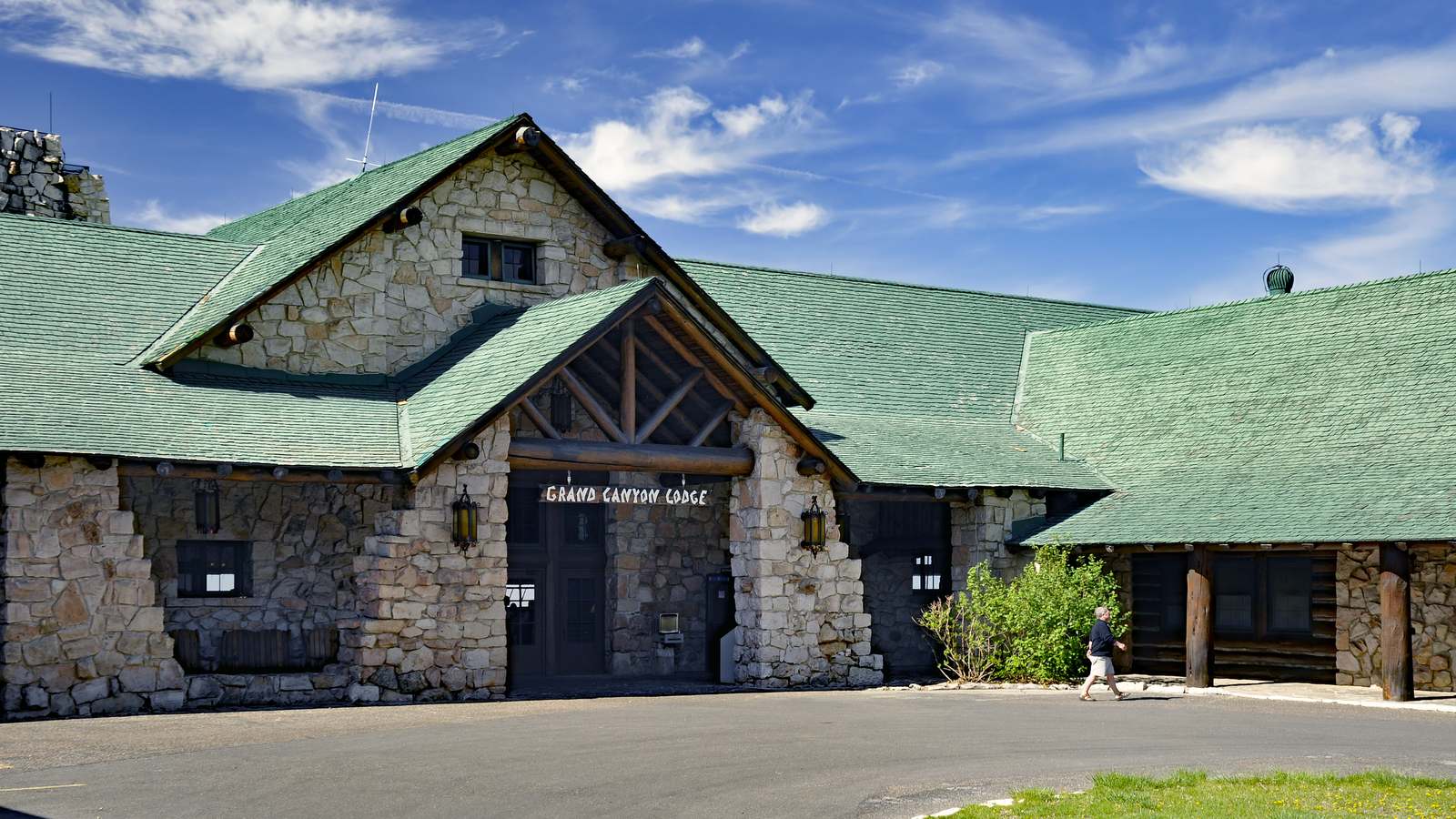 The stone and timber entrance of Grand Canyon Lodge on the North Rim under a blue sky, with a green shingle roof.