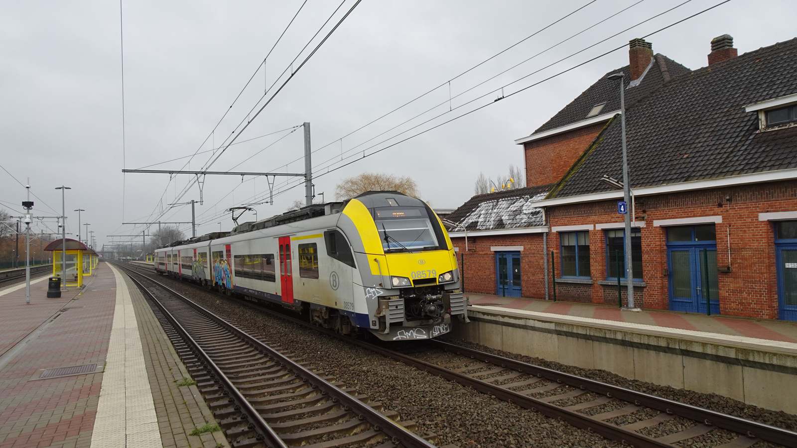 An SNCB S1 double-deck train at the platform of Duffel station beside the brick station building