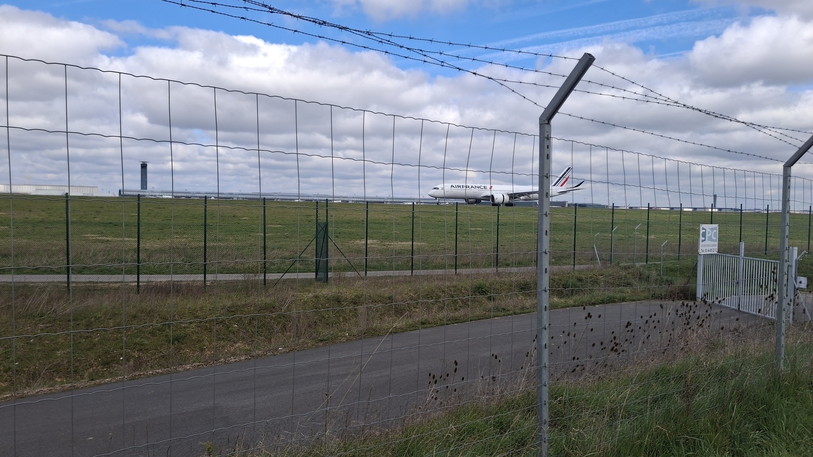 Air France Airbus A350 on the grass at Paris Charles de Gaulle, seen through a perimeter fence under a cloudy sky