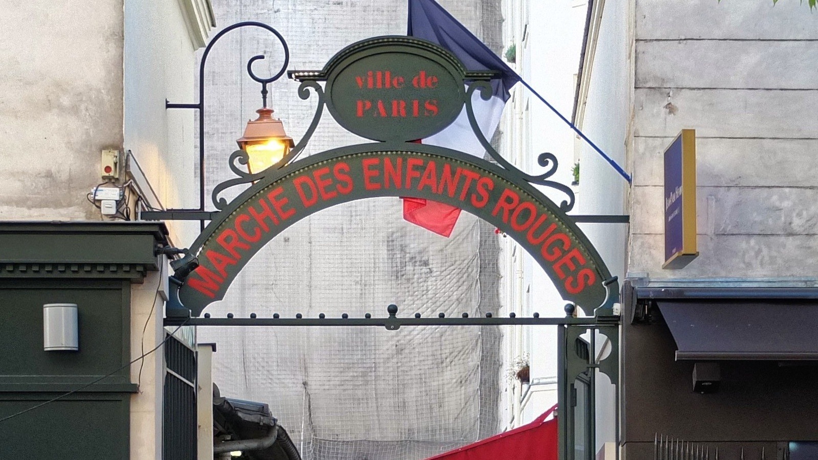 Green iron entrance arch reading Marche des Enfants Rouges with a Ville de Paris plaque, lantern and French flag, in a May 2016 file photo