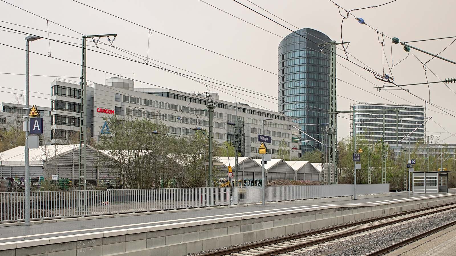 Platform at Stuttgart-Vaihingen station with the station name sign and office towers behind