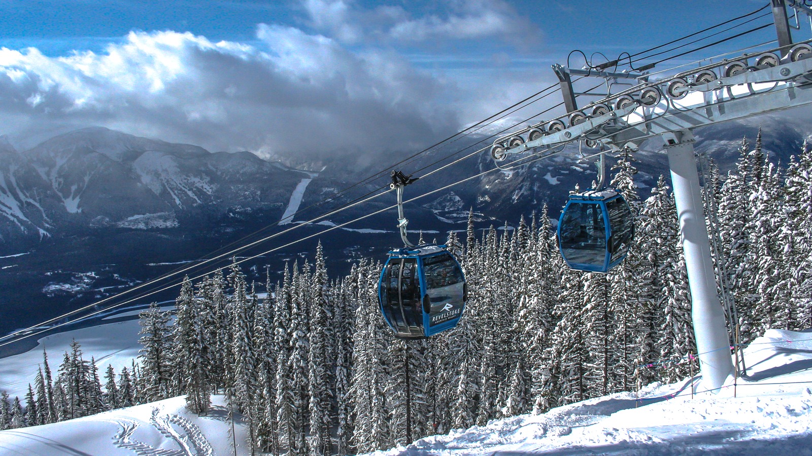 Blue Revelstoke gondola cabins over snow-covered pines with the Columbia Valley and mountains beyond
