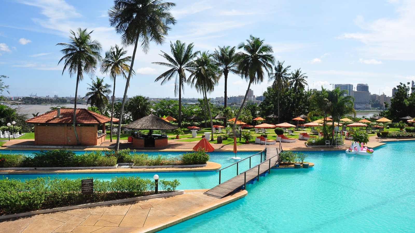Pool and palm gardens at Hotel Ivoire in Abidjan, Cote dIvoire, with the city skyline across the lagoon