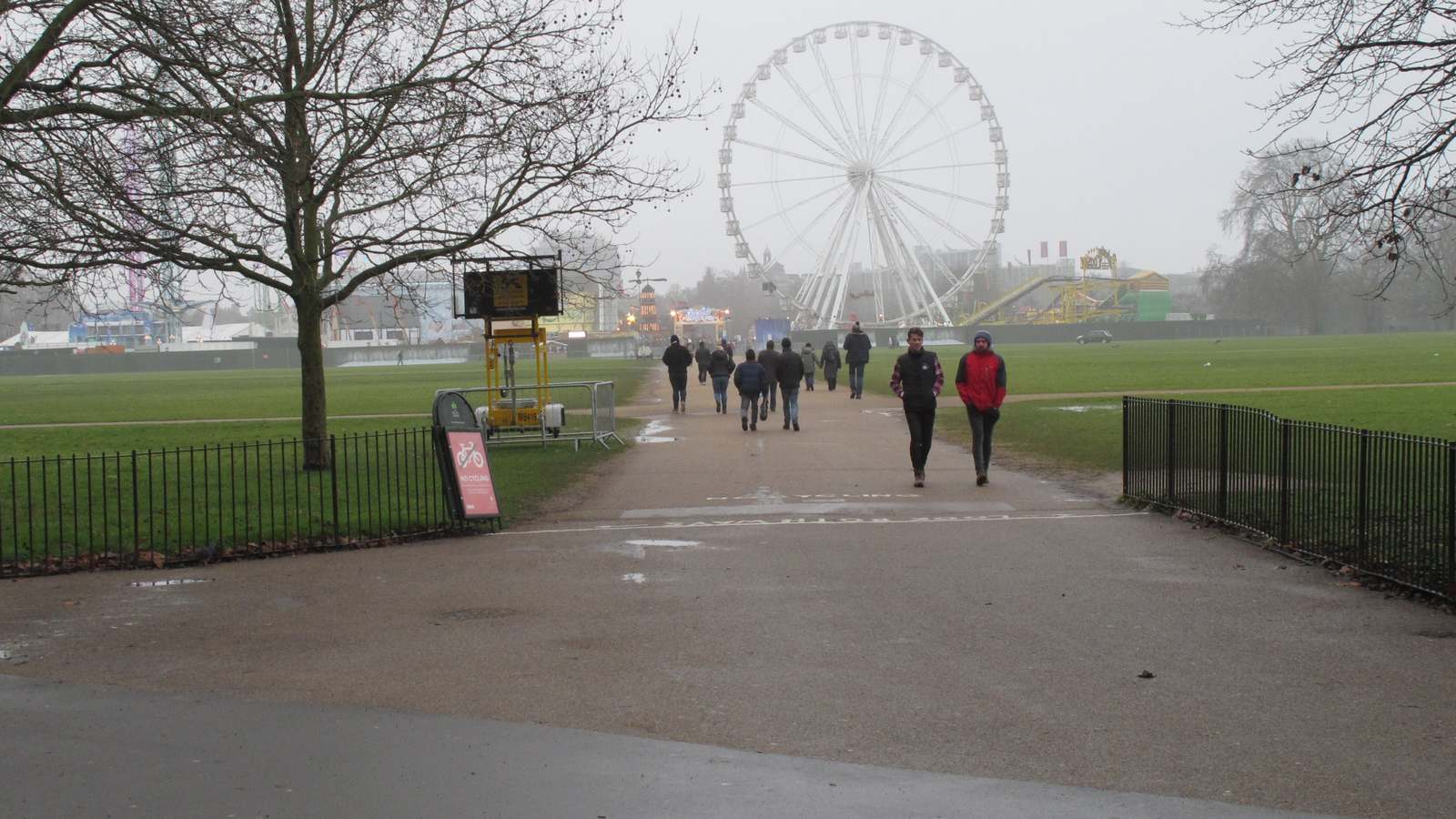 Visitors walking along a Hyde Park path toward Winter Wonderland and its Giant Wheel