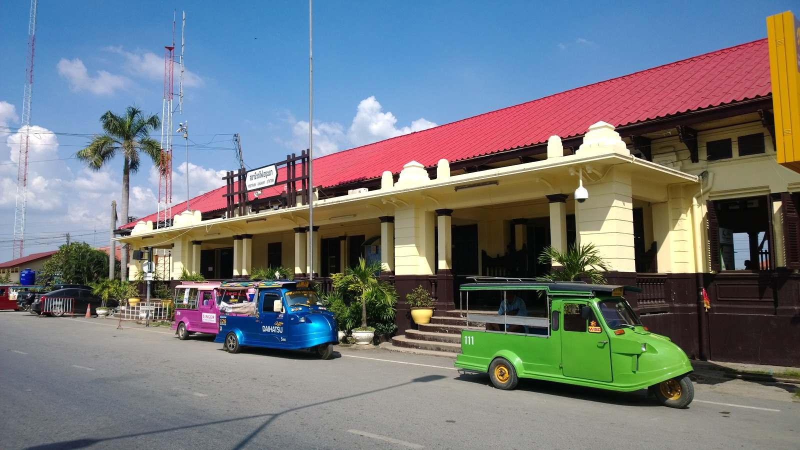 Cream-and-red Ayutthaya railway station with tuk-tuks parked along the street in Phra Nakhon Si Ayutthaya, Thailand
