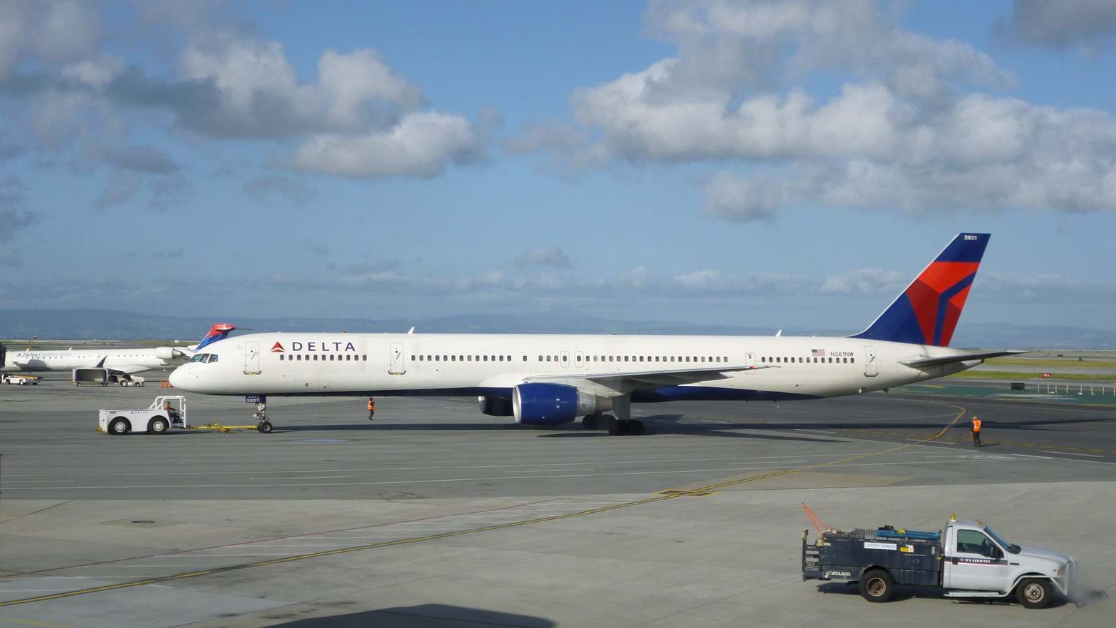 A Delta Air Lines Boeing 757 being pushed back on the ramp at San Francisco International Airport under a partly cloudy sky.