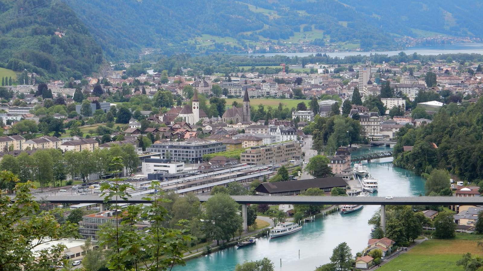 Interlaken seen from above with Interlaken Ost station, its tracks and the turquoise Aare canal lined with lake boats