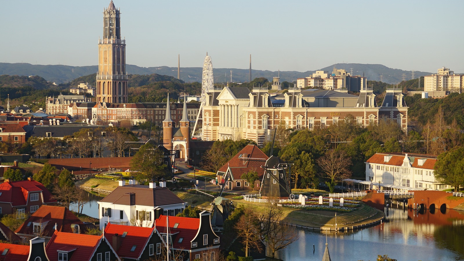 Huis Ten Bosch theme park in Sasebo, Nagasaki, with canals, windmills, red-roof houses, and the Domtoren replica tower in daylight