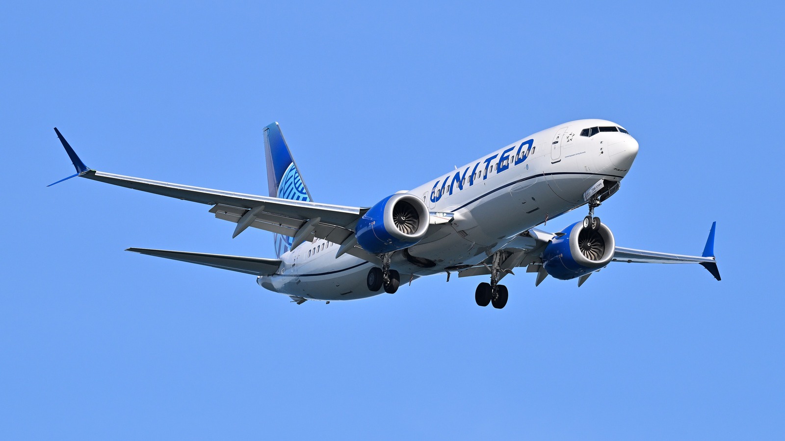 A United Airlines Boeing 737 MAX 8 on final approach against a clear blue sky