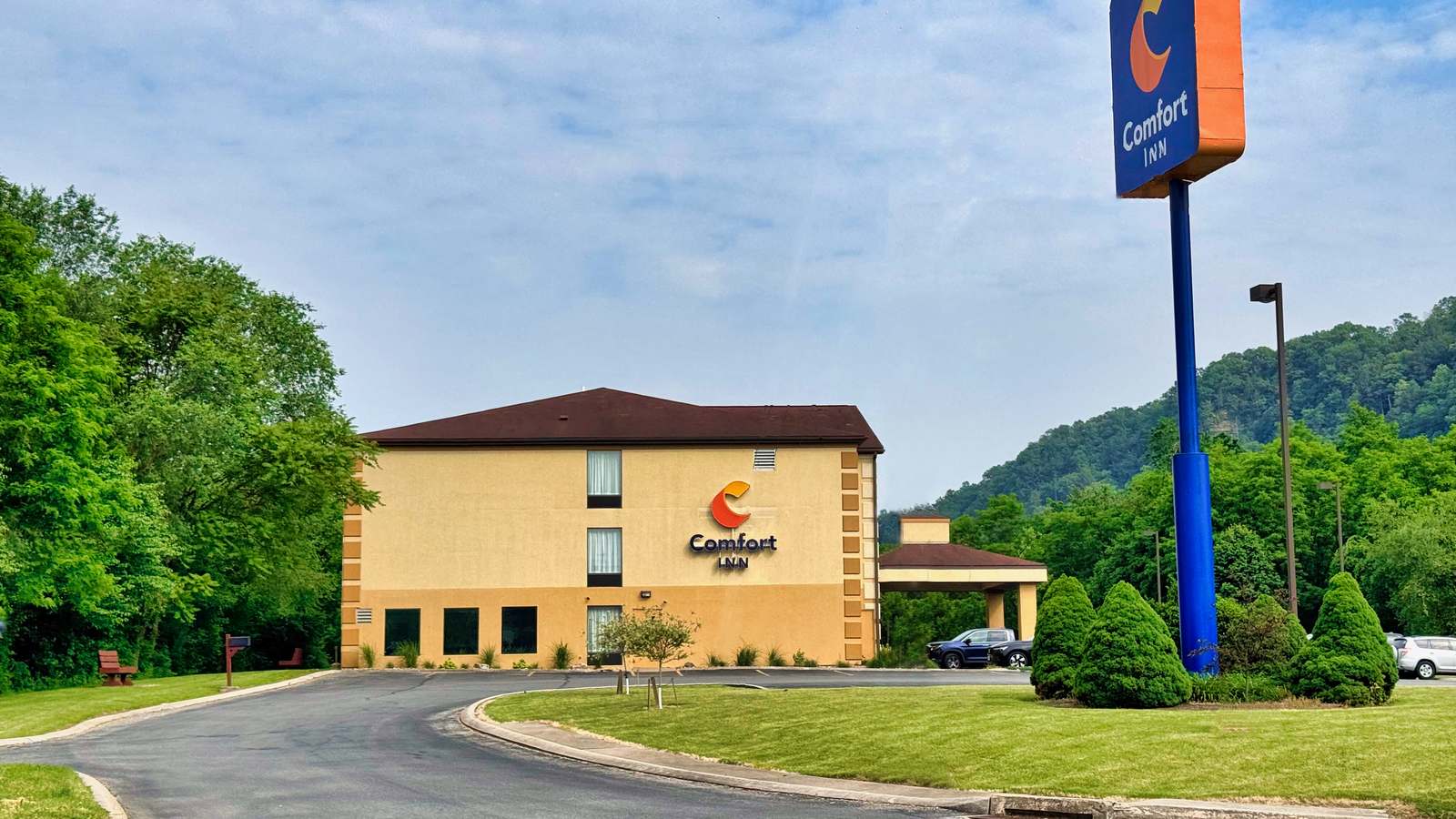 A Comfort Inn hotel with its tall roadside sign beside wooded hills under a blue sky in Huntingdon, Pennsylvania.