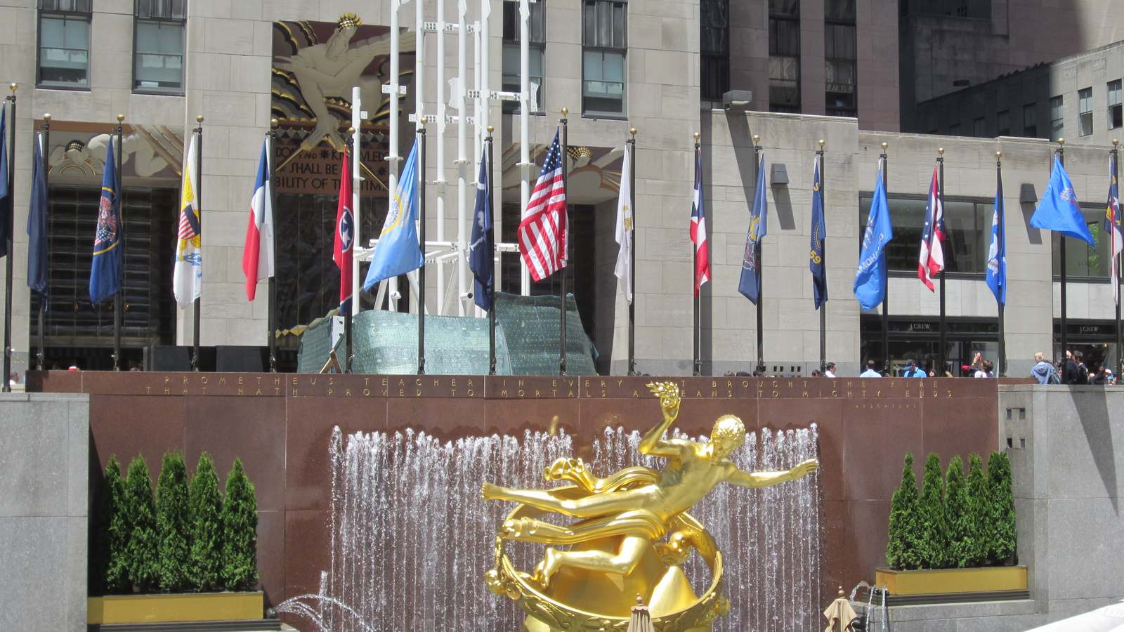 The golden Prometheus statue and fountain at Rockefeller Center's Lower Plaza with a row of flags, photographed in May before the ice rink season.
