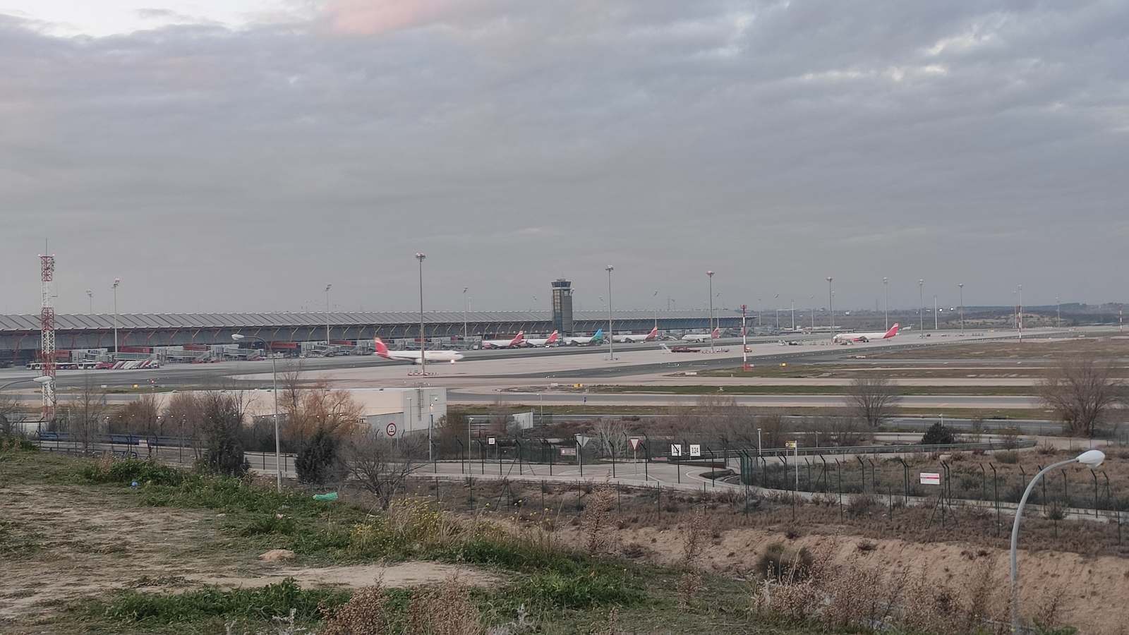 Madrid Barajas Terminal 4 and its control tower with parked aircraft under a cloudy sky