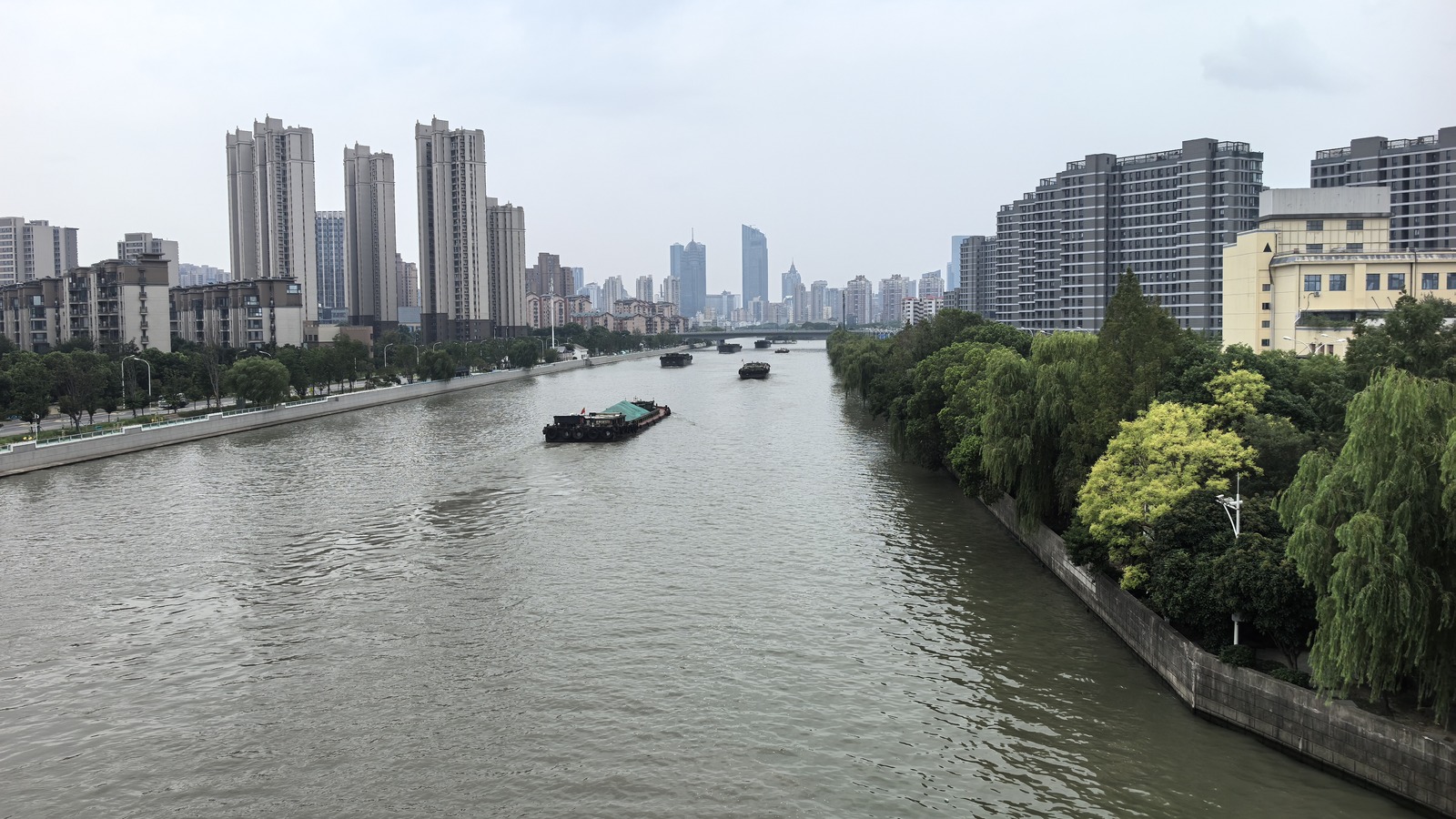 Barges on the Grand Canal in Liangxi District, Wuxi, Jiangsu, with high-rises along both banks under an overcast sky