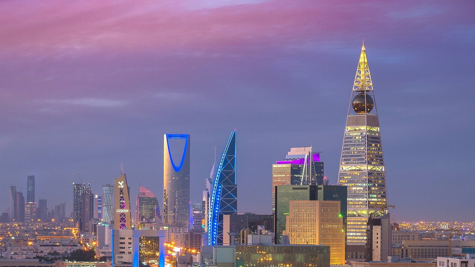 The Riyadh skyline at dusk with Kingdom Centre and Al Faisaliah Tower lit against a purple sky