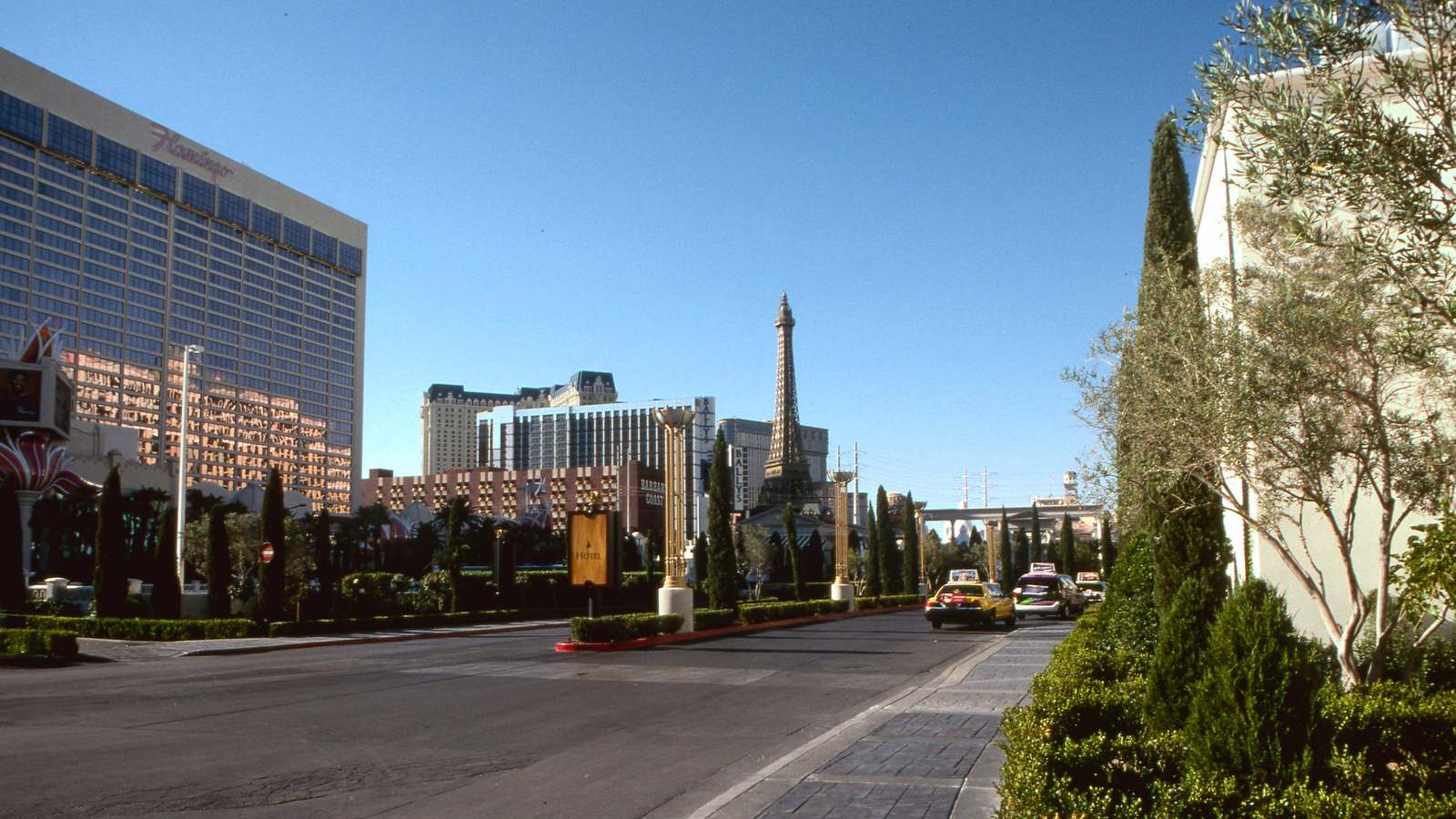 The Flamingo Las Vegas hotel tower on the Strip on a sunny day, with the Paris Las Vegas Eiffel Tower replica in the distance.