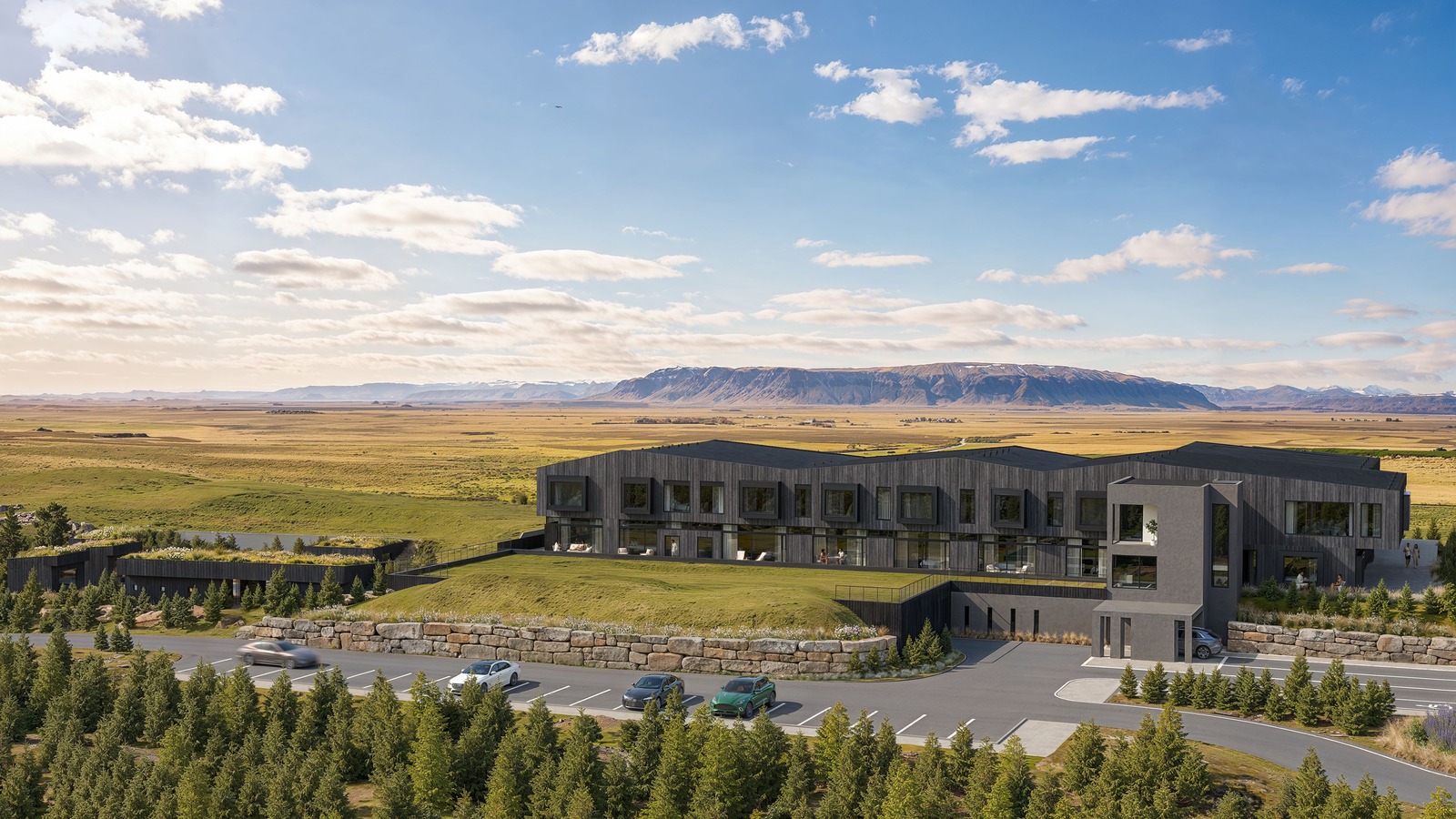 360 Hotel in South Iceland, a dark timber lodge with grass roofs facing mountains beyond a parking court