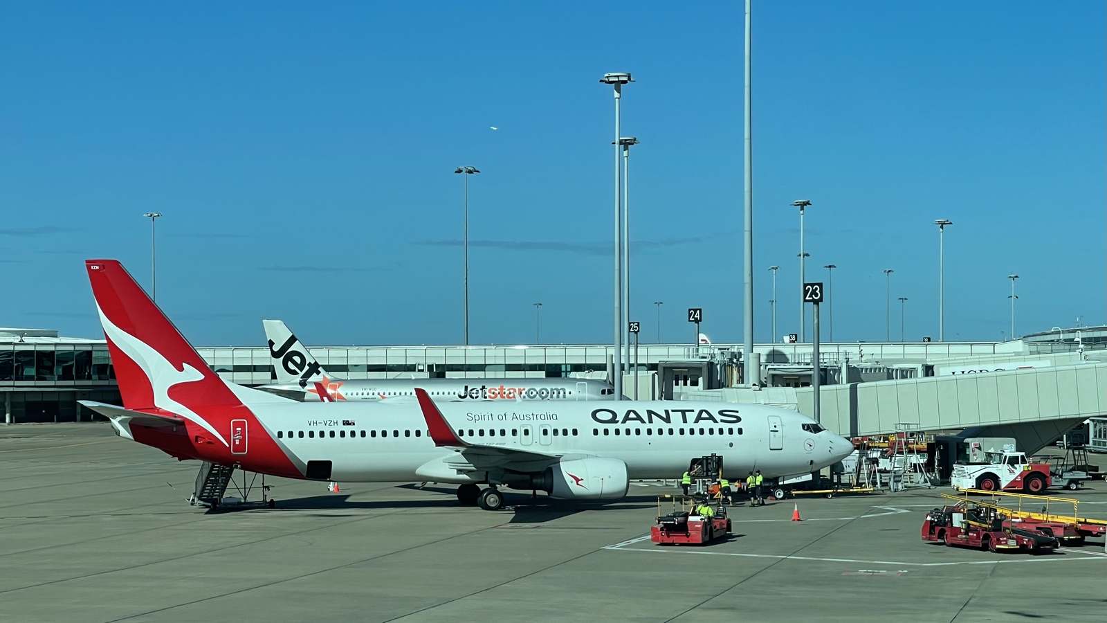 A Qantas Boeing 737 in red and white livery parked at a gate at Brisbane Airport's domestic terminal on a clear day.
