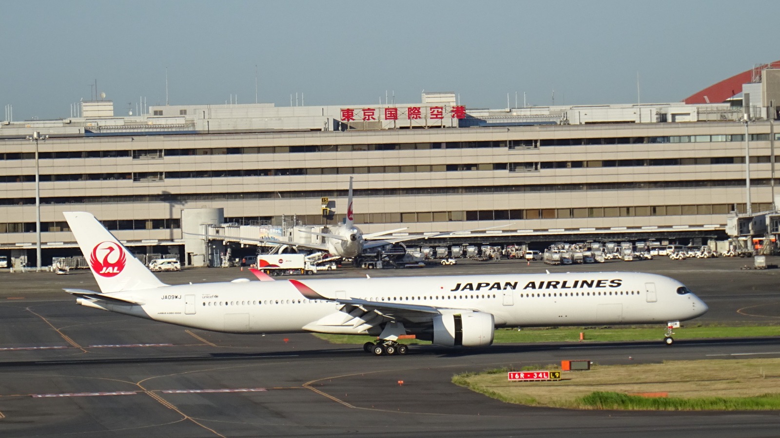 A Japan Airlines Airbus A350-1000 in white livery with the red crane logo taxiing past the terminal at Tokyo Haneda Airport.
