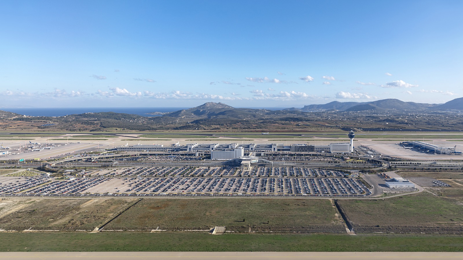 Aerial view of Athens International Airport Eleftherios Venizelos, showing the terminal, parking lots, runways, control tower, mountains and the sea, photographed in December 2019.