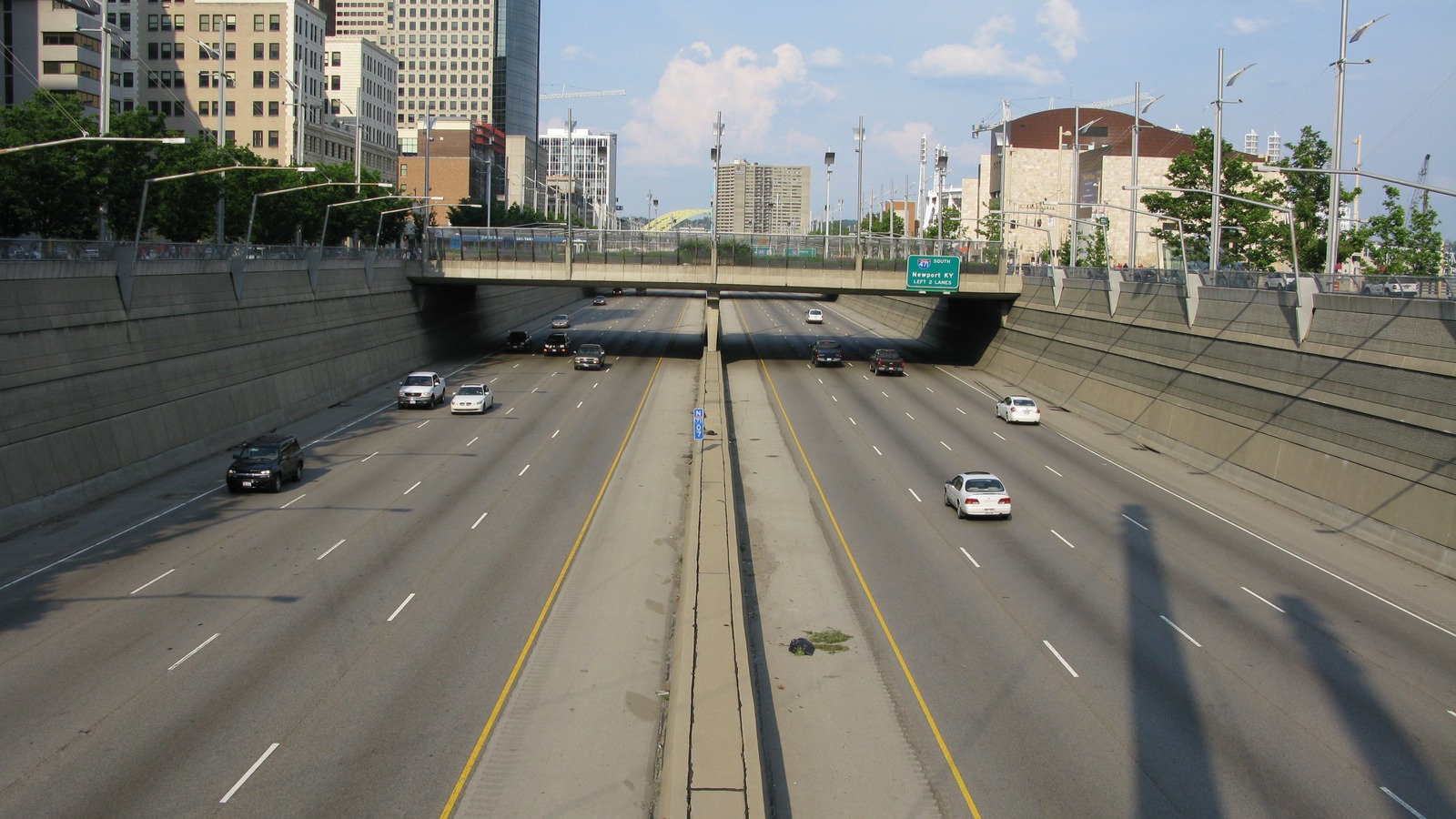 Traffic in the sunken Fort Washington Way freeway trench in downtown Cincinnati, with an I-471 South sign over the lanes and the city skyline beyond.