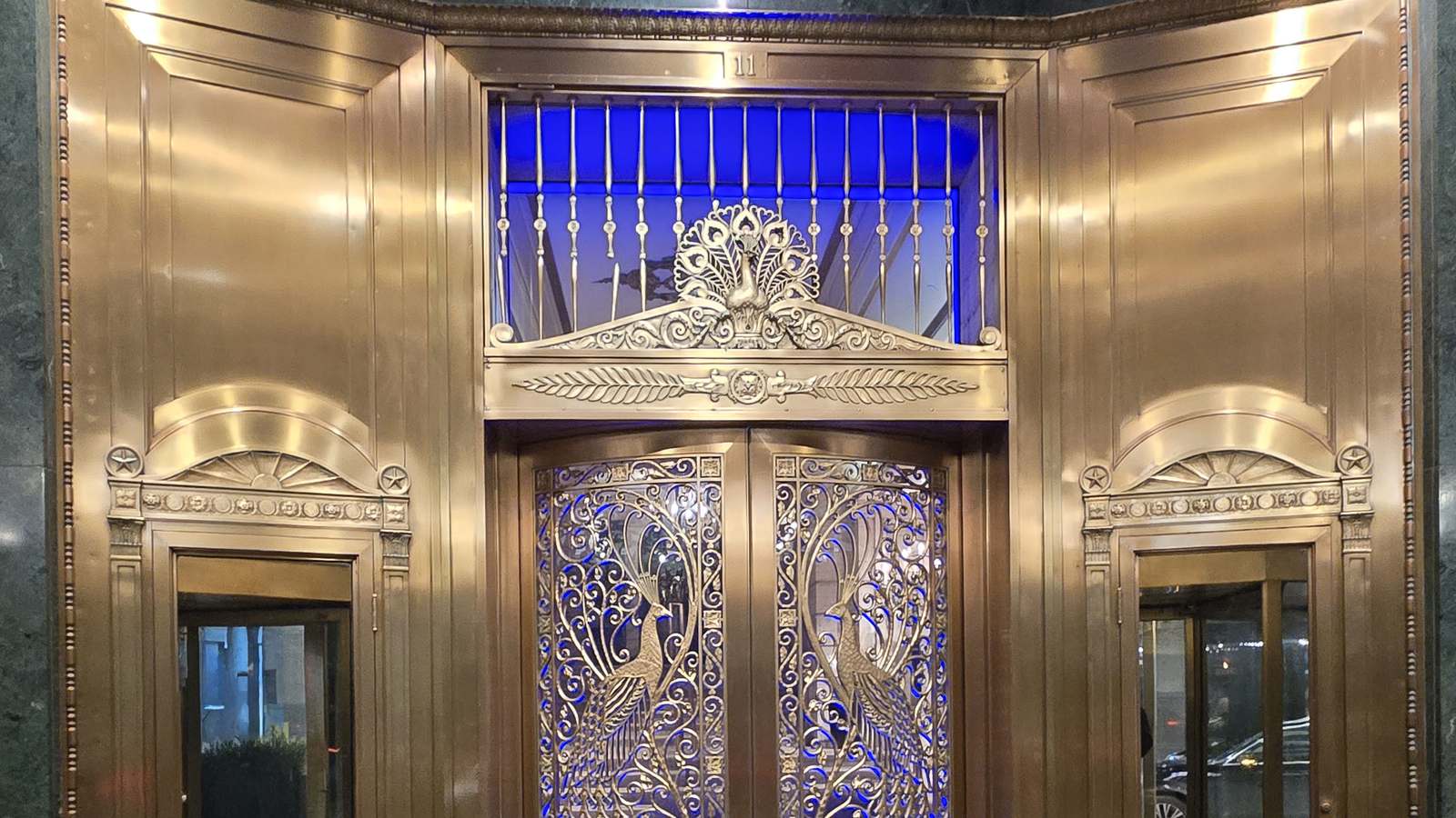 The ornate brass Peacock Door entrance of the Palmer House Hilton in Chicago, with peacock metalwork lit in blue.
