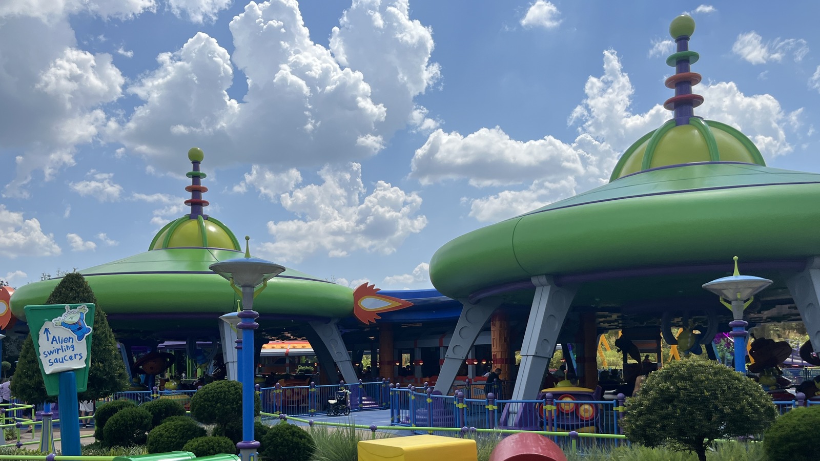 Daytime exterior of Alien Swirling Saucers in Toy Story Land at Disney Hollywood Studios, with green saucer roofs and a ride sign.