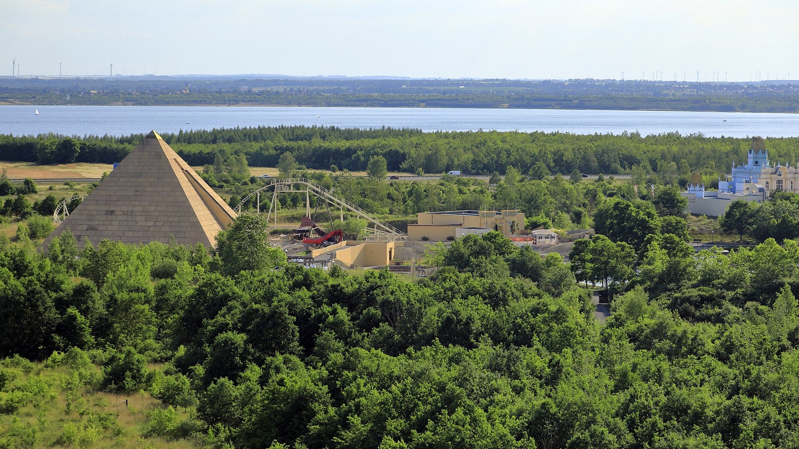 The pyramid and blue castle building of BELANTIS theme park near Leipzig seen from a lookout over trees and a lake