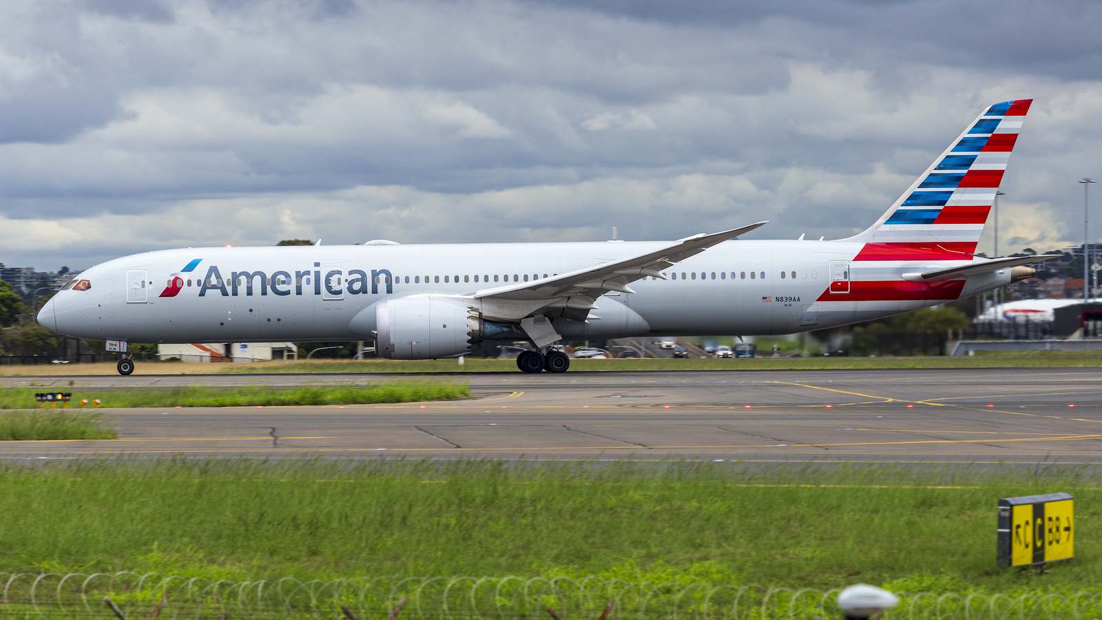 An American Airlines Boeing 787-9 rolls along the runway at Sydney Airport under a cloudy sky.