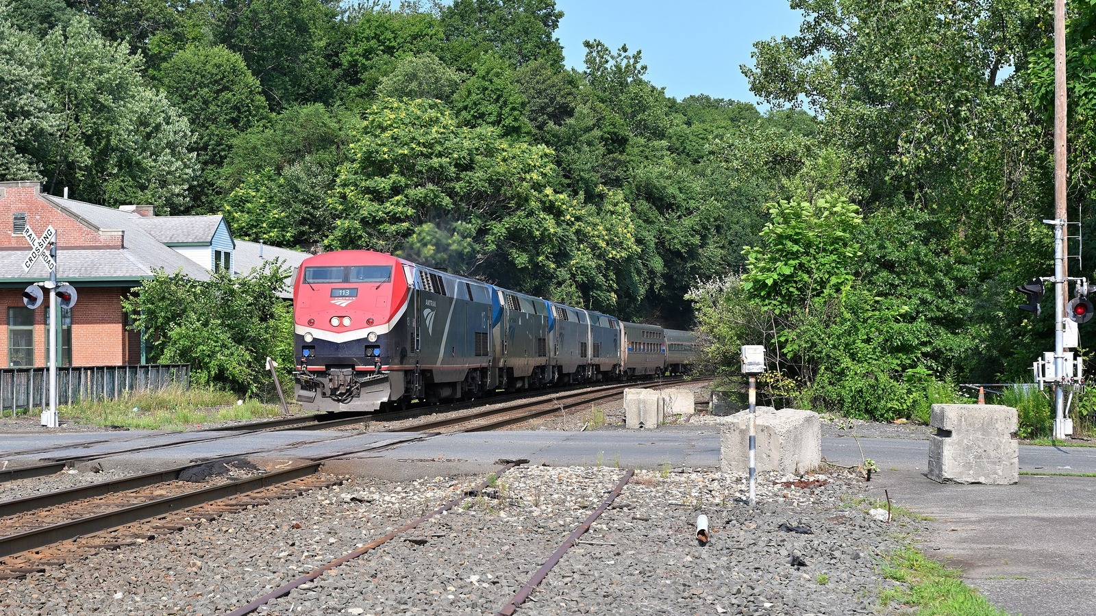 An Amtrak passenger train with a red-nosed locomotive approaches a grade crossing in West Springfield, Massachusetts, in August 2026