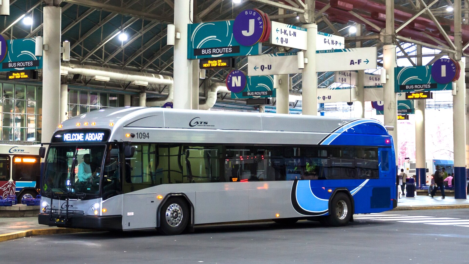 A silver and blue CATS city bus at a bus bay with route signs overhead