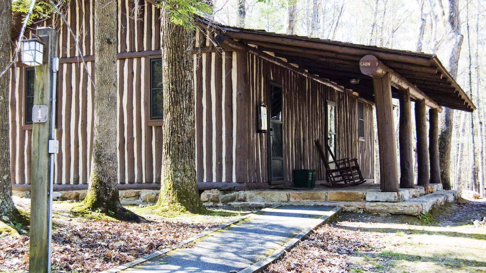 A rustic log cabin with a covered porch and rocking chair among bare trees, shown as an example of a vacation rental cabin.