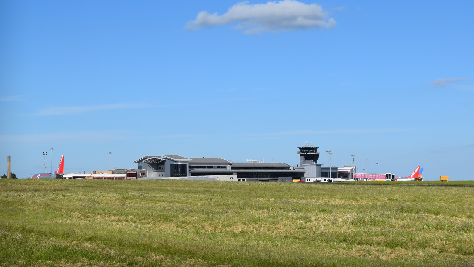 Leeds Bradford Airport terminal, control tower and parked aircraft seen across the airfield on a clear day