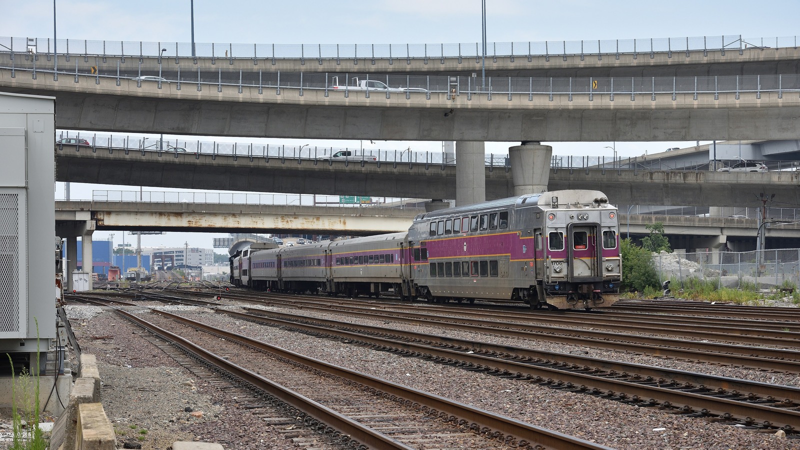 MBTA Commuter Rail train with a purple and gray cab car leaving the North Station area under Boston highway overpasses