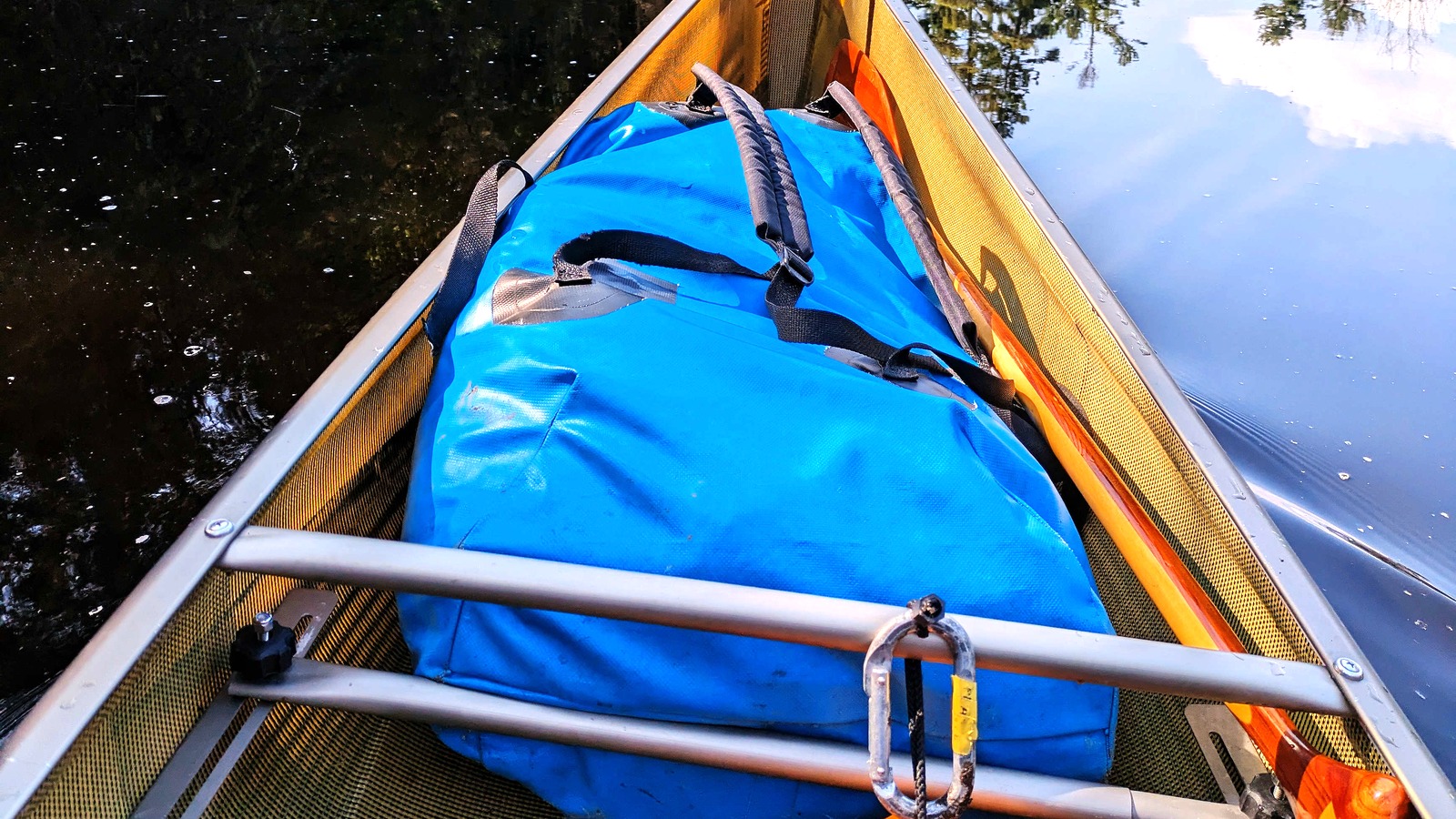 A large blue dry bag secured in a canoe on calm water.