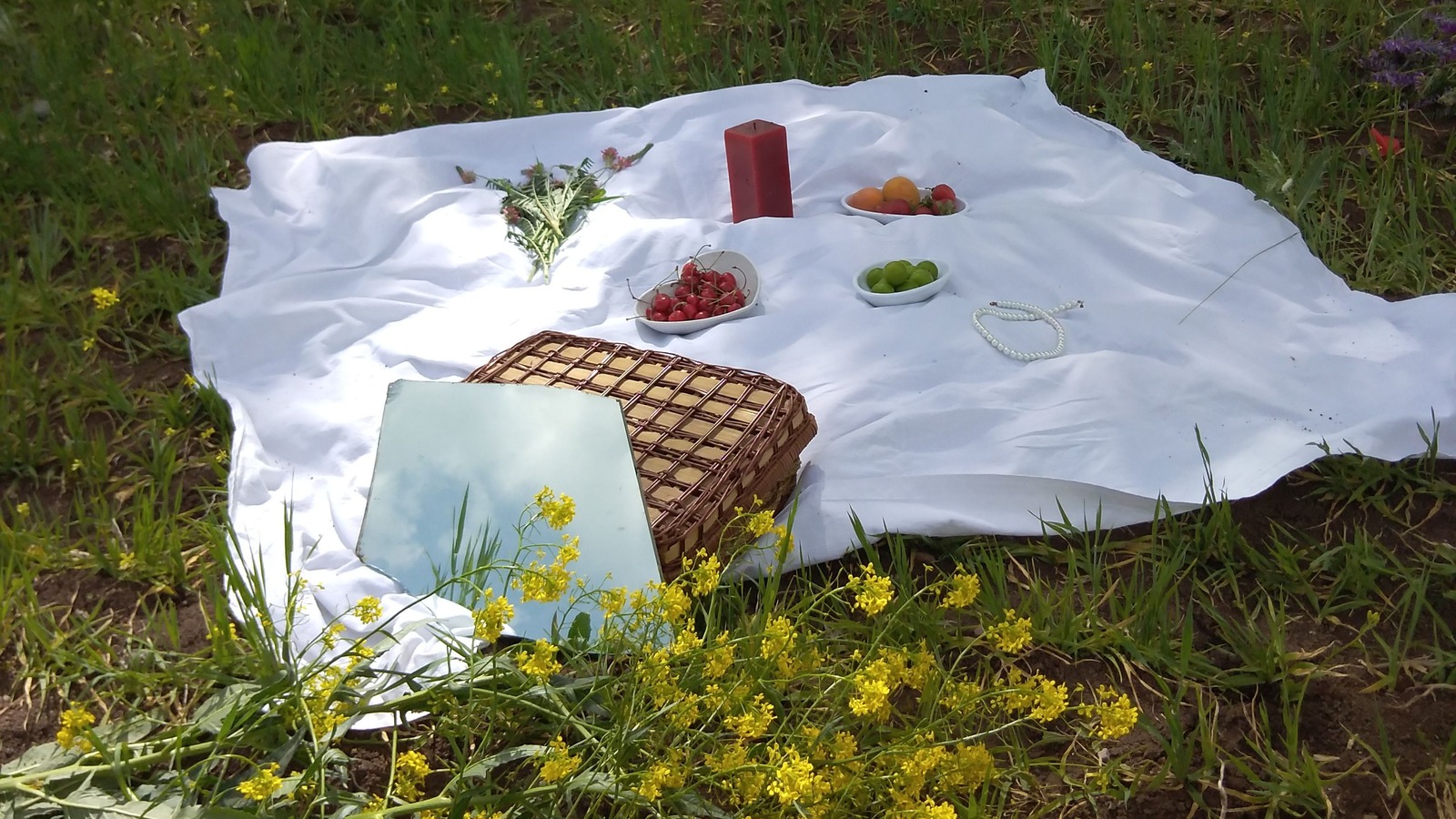 A white picnic blanket spread on grass with a picnic basket, fruit and food.