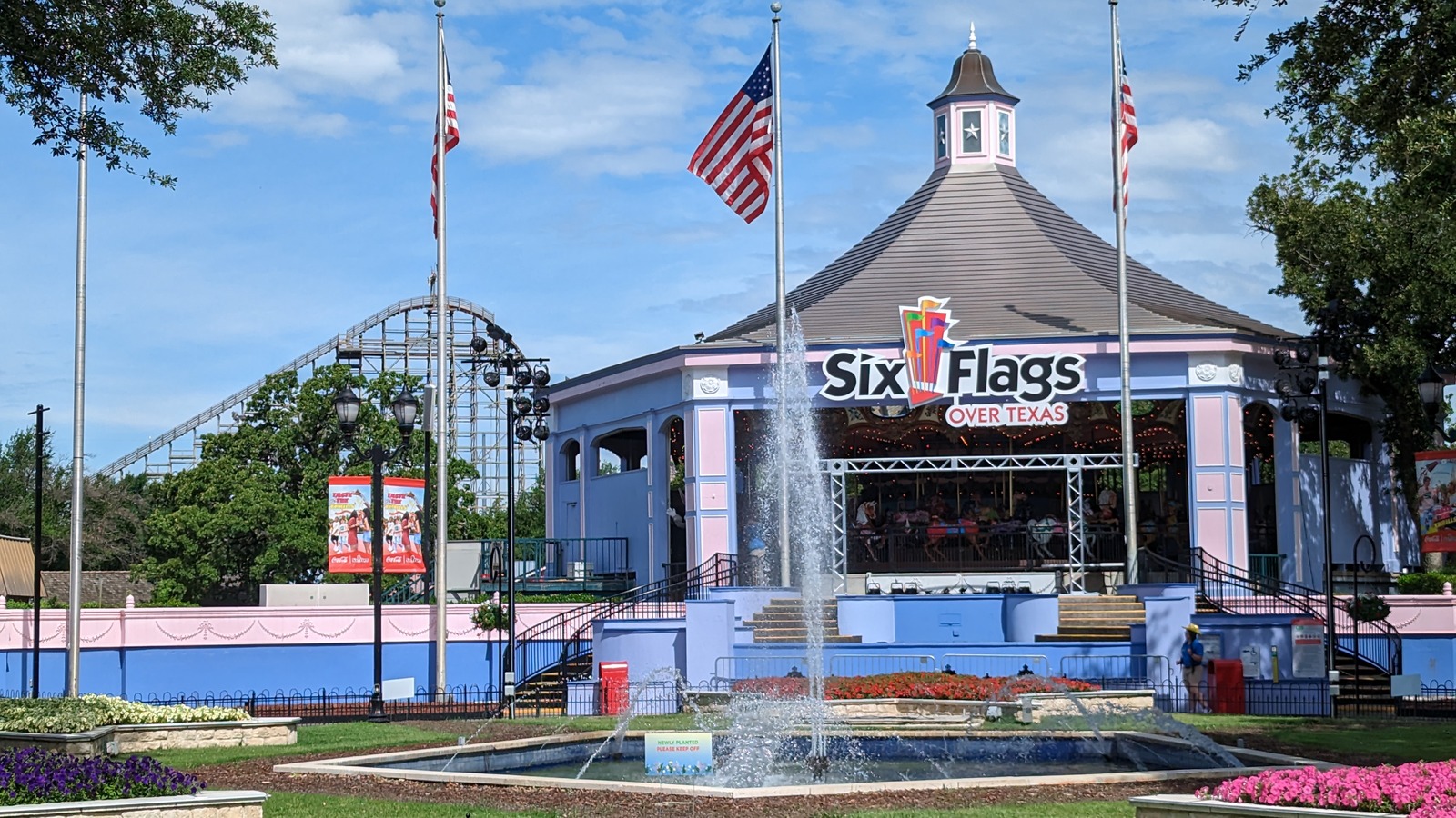 Six Flags Over Texas pavilion with the park name above a landscaped fountain and coaster track behind it