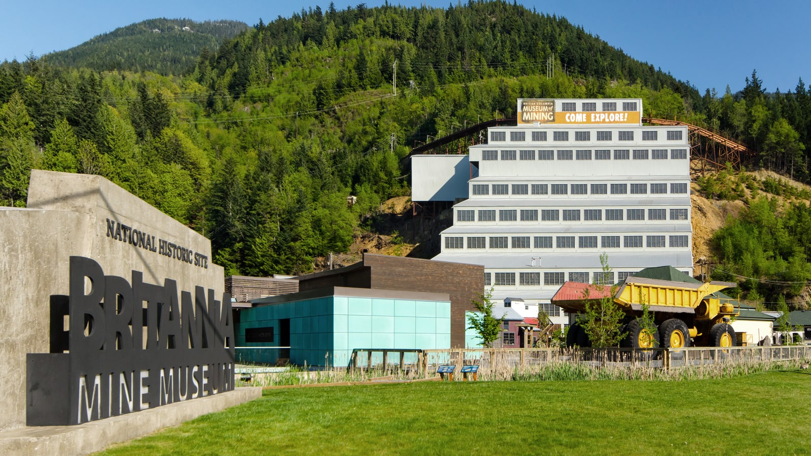 Britannia Mine Museum buildings and a yellow mining truck below a forested mountainside.